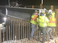 Workers assist crane to guide beam into place.